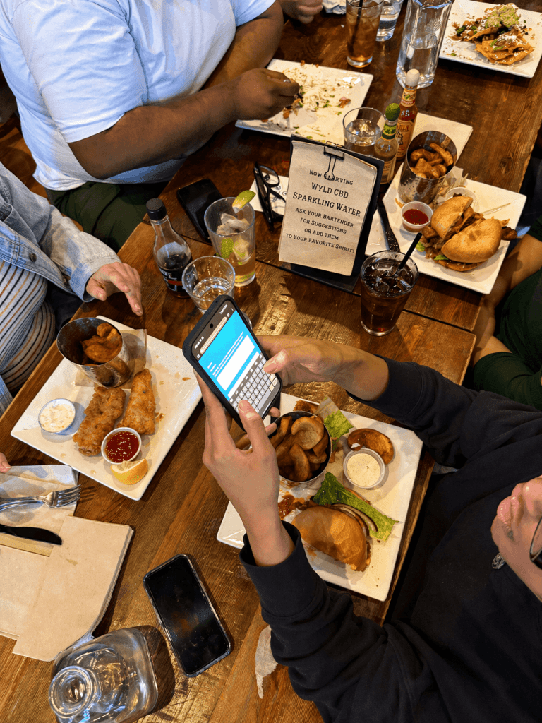 Friends answering trivia questions on a phone at a bar table with food and drinks